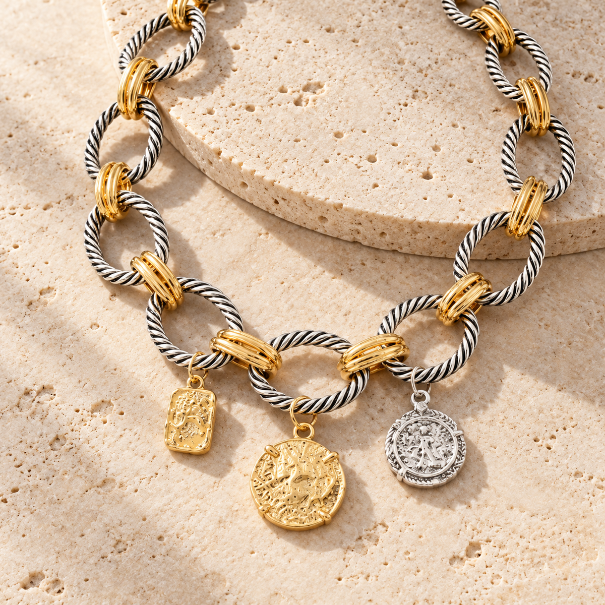 AI-assisted flat lay of the mixed-tone necklace with three charms on warm stone