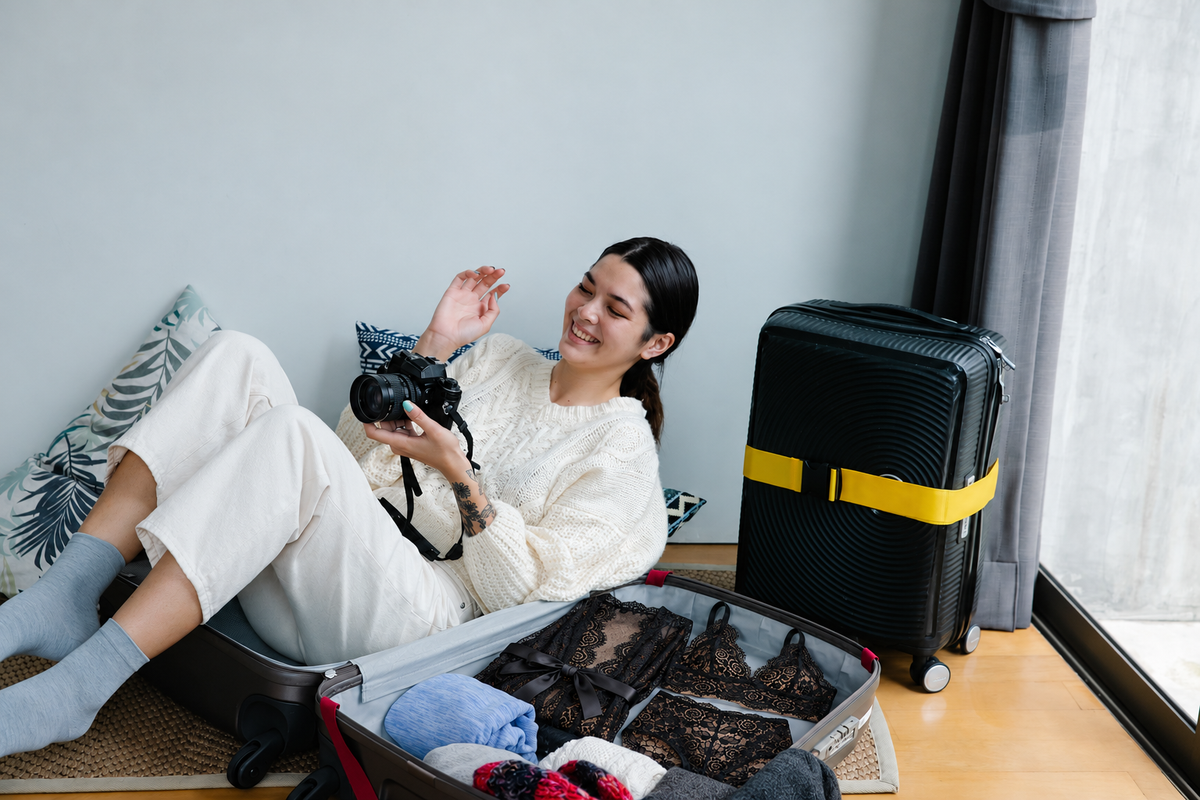 Travel editorial showing the black three-piece lace set packed in an open suitcase beside a clothed model