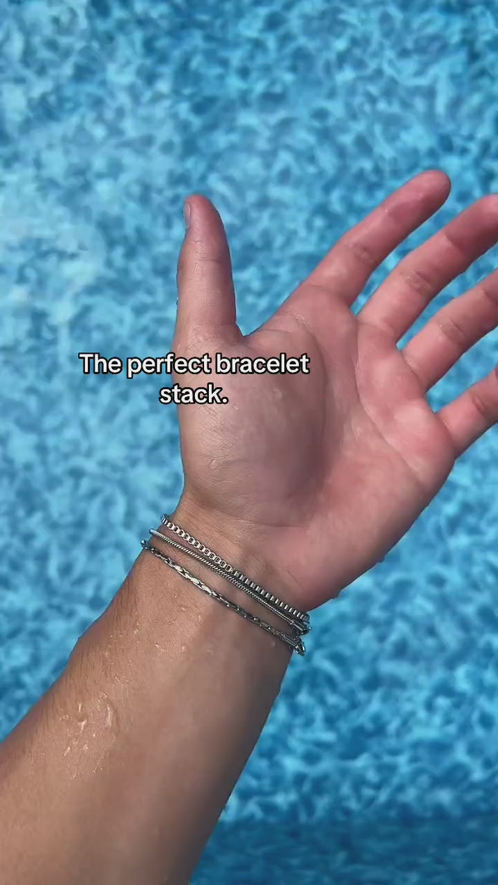 Three-chain Veyron bracelet stack shown on a wrist over blue pool water