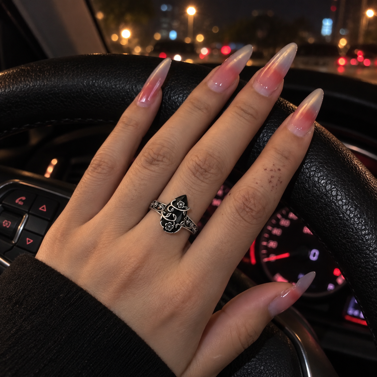 Pink-manicured hand wearing the floral ring on a steering wheel at night